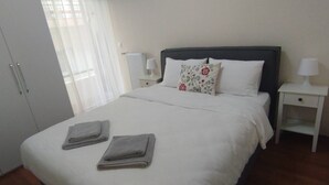 A neatly made bed with two folded towels, a bedside table with a lamp, and a radiator. - Seizani Athens Stay-1,6 km from Panathenaic Stadium (Kaisariani)