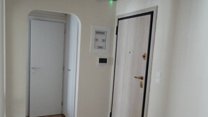 A hallway with a marble floor, a white door with a black frame, and a wall-mounted emergency exit sign. - Seizani Athens Stay-1,6 km from Panathenaic Stadium (Kaisariani)