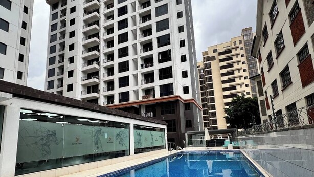 Una piscina con suelo de baldosas, rodeada de edificios residenciales altos.