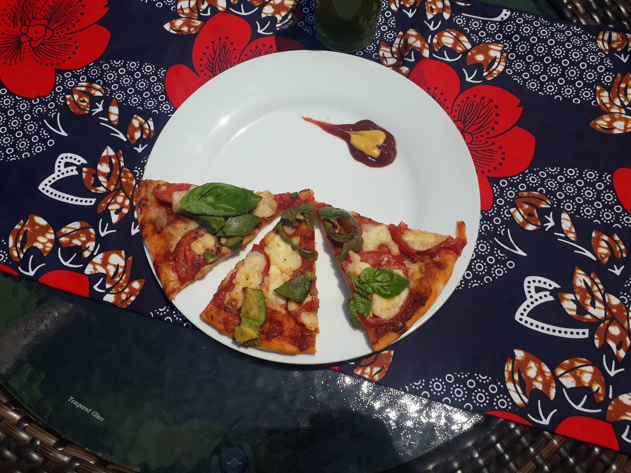 Ein Teller mit Pizzastücken und etwas Soße auf einer Tischdecke mit Blumenmuster.
