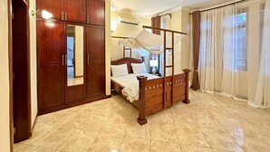 Quarto com cama de dossel, guarda-roupa e uma grande janela com cortinas.