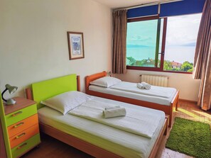 Una habitación con dos camas, una mesita de noche con lámpara, un cuadro en la pared y una ventana con vistas.