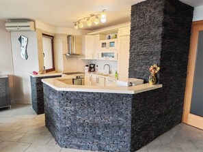 A modern kitchen with a stone accent wall, a built-in island, and a hanging light fixture. - Villa Vrata Jadrana 1 (Rijeka)