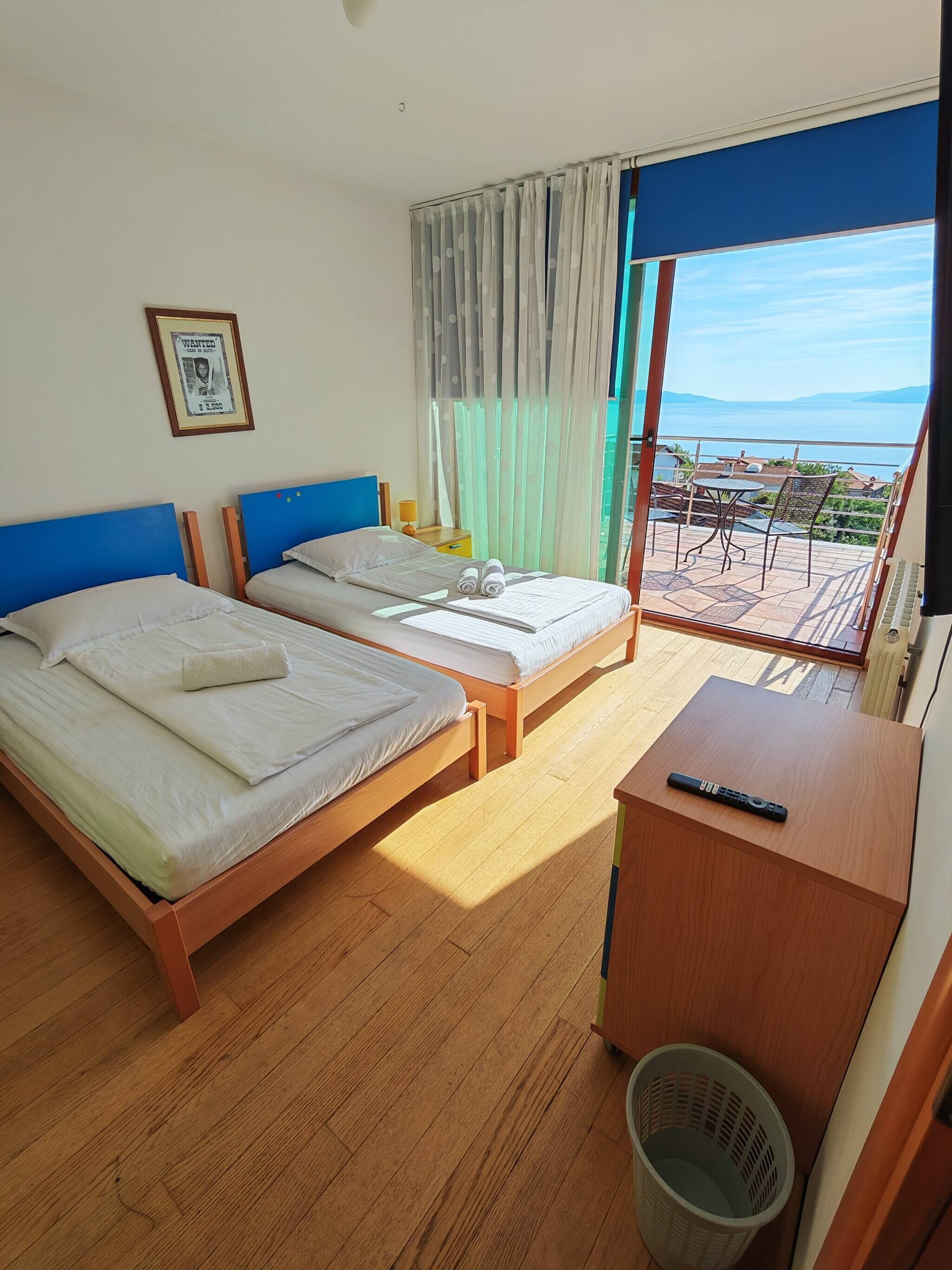 A hotel room with two beds, a small desk, a remote control, and a view of the sea.