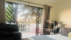 A bedroom with a bed, a chair, a desk, and a view through a large window. - 3 bed Cluster home in Sandton (Sandton)