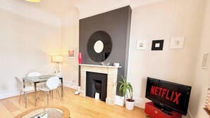 Ett modernt vardagsrum med en öppen spis, en matplats och en tv-skärm som visar ”NETFLIX”.