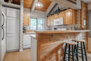 A kitchen with wooden cabinets, a white refrigerator, a microwave, a stove, and two bar stools. - Wildflower 60: Nice, Centrally Located (Mammoth Lakes)