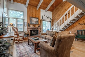 A cozy living room with a fireplace, wooden walls, a staircase, and a large window. - Wildflower 60: Nice, Centrally Located (Mammoth Lakes)