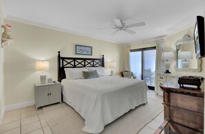 Ein Schlafzimmer mit Bett, Nachttischen, einem Schminktisch, einem Deckenventilator und einem Fenster mit Vorhängen.