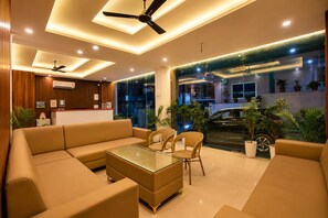 A modern hotel lobby with a sofa set, a glass-top coffee table, wicker chairs, ceiling fans, and a view of the street outside. - SUNBURRY HOTEL TAPOVAN RISHIKESH (Rishikesh)