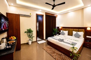 A hotel room with a bed, bedside table, TV, air conditioning unit, and a door leading to a bathroom. - SUNBURRY HOTEL TAPOVAN RISHIKESH (Rishikesh)