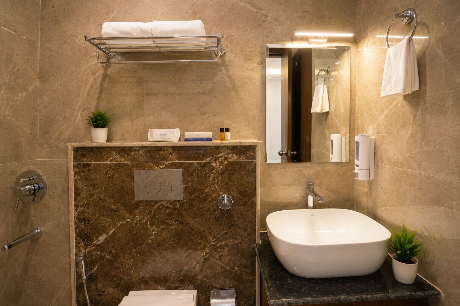 Une salle de bain moderne avec un mur en marbre, un lavabo sur pied, un porte-serviettes et une petite plante en pot.