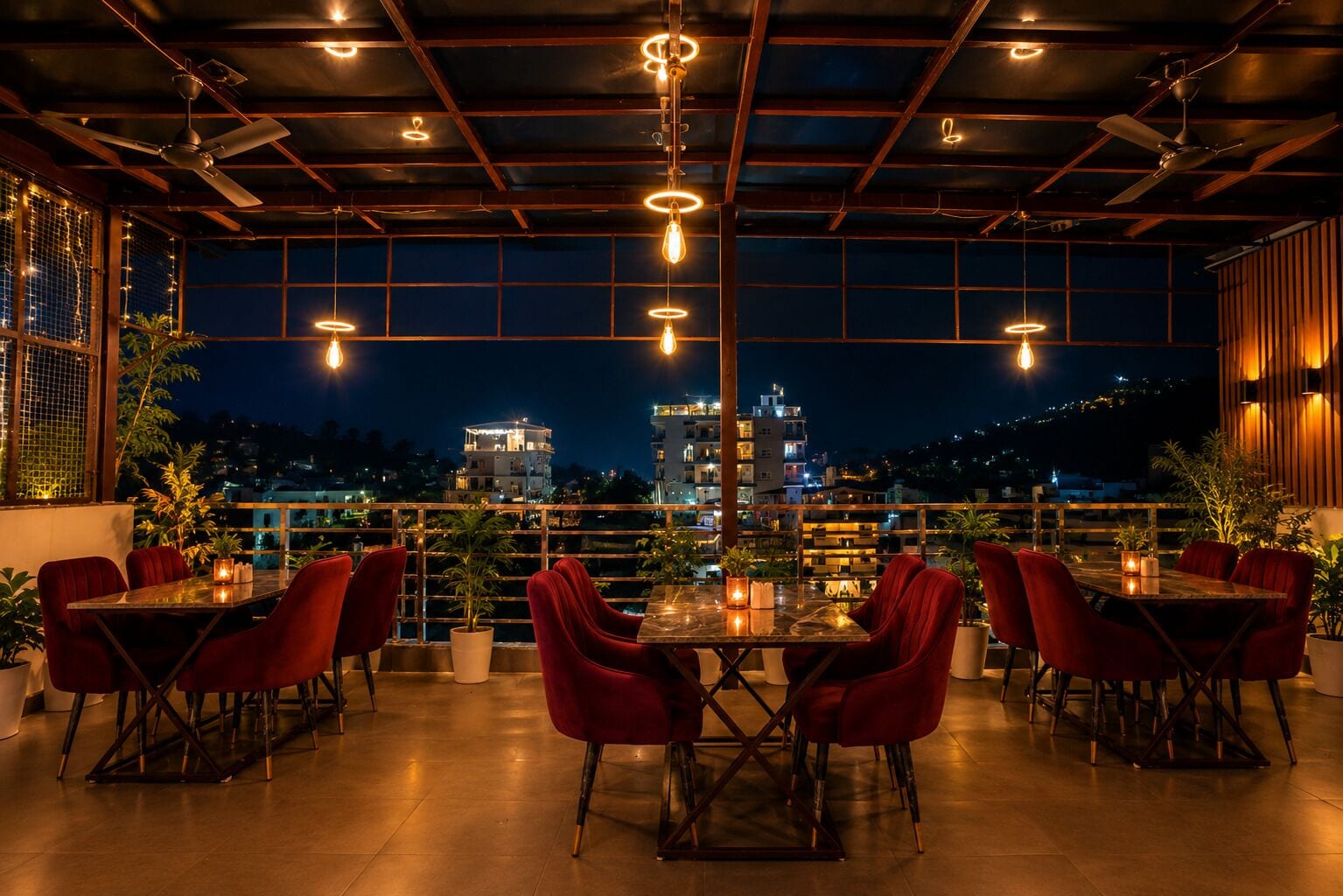 Un espacio al aire libre para comer con mesas y sillas, iluminación colgante y vistas de edificios al fondo.