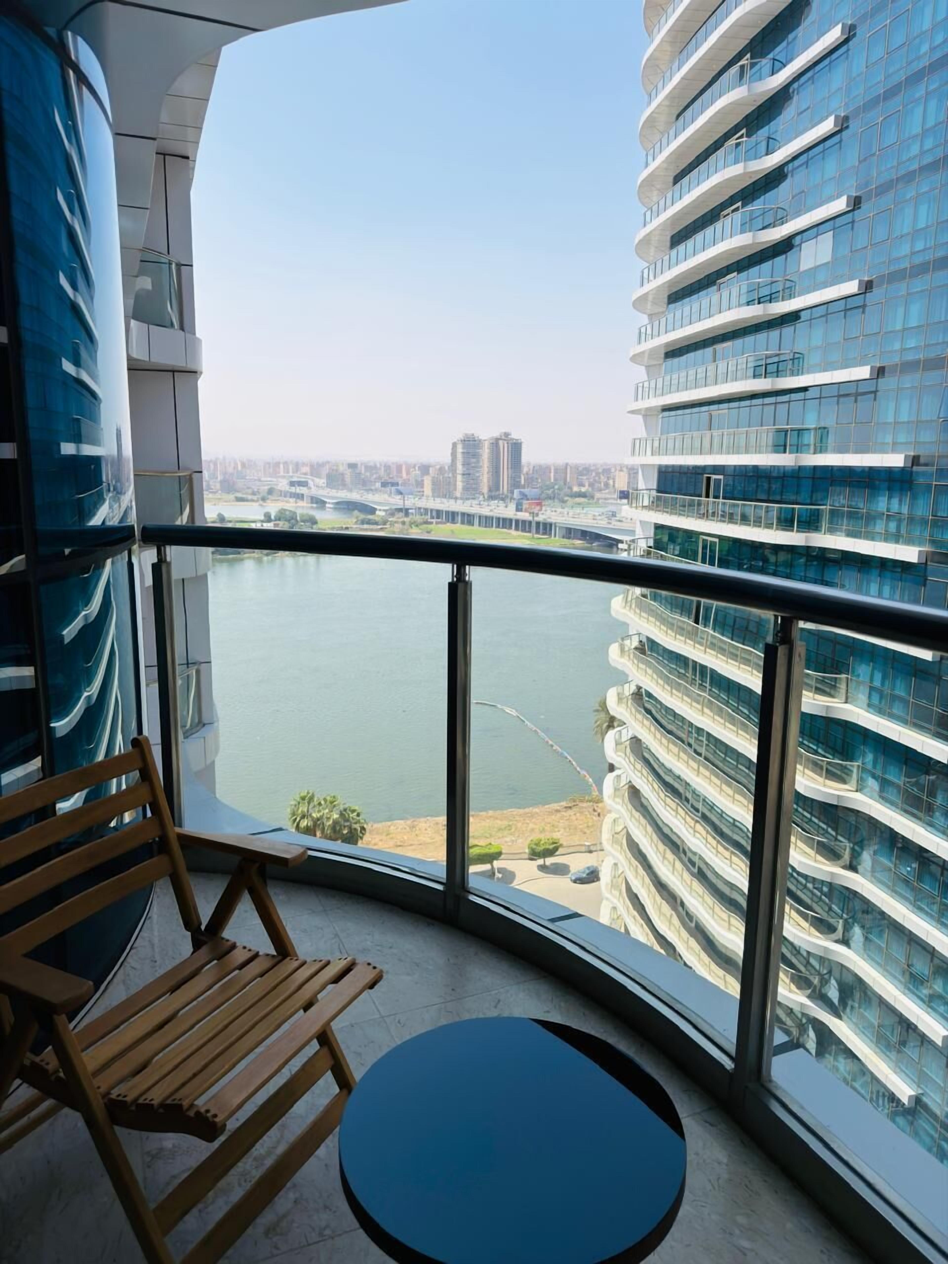 A balcony with a view of a river and cityscape, a wooden chair, and a small table.