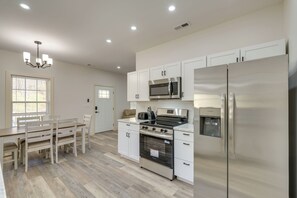 Eine moderne Küche mit weißen Schränken, Edelstahlgeräten, einem Essbereich mit Holztisch und Stühlen sowie einer Kandelaberleuchte.