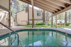 A swimming pool with a tiled edge, a wooden deck, and a building with a tiled exterior in the background. - Condo 1 Mi to Village | Pool + Resort Amenities (Mammoth Lakes)