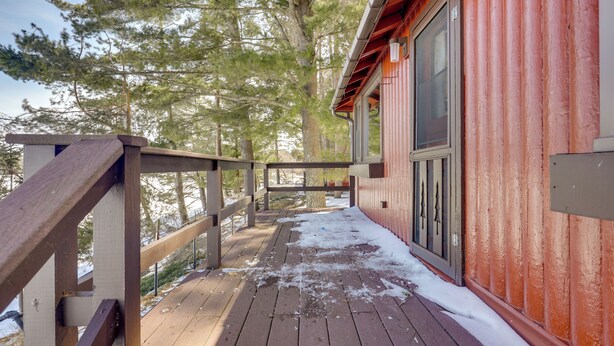 A wooden deck with snow on the ground, a red building with a window, and a wooden railing. - Peaceful Lakefront Cabin, 5 Mi to Dtwn Minocqua! (Arbor Vitae)