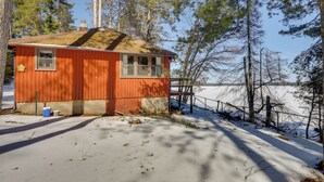 A small, single-story cabin with a sloped roof, a window, and a door, surrounded by snow and trees. - Peaceful Lakefront Cabin, 5 Mi to Dtwn Minocqua! (Arbor Vitae)