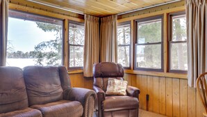 A room with wooden walls and large windows, featuring two leather sofas and a recliner. - Peaceful Lakefront Cabin, 5 Mi to Dtwn Minocqua! (Arbor Vitae)