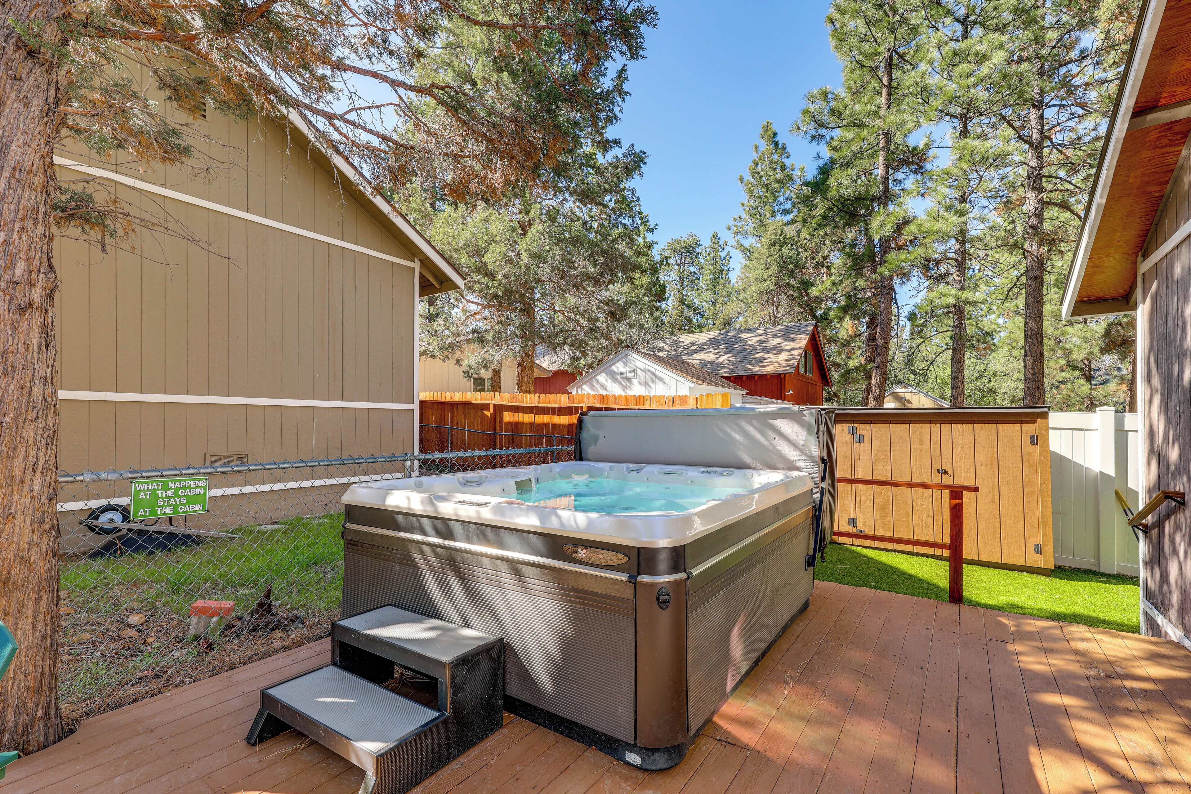 A hot tub on a wooden deck with a wooden fence and trees in the background.