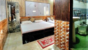 Quarto com cama, espelho, parede de pedra, ventoinha no teto e banheiro visível através de uma porta aberta.