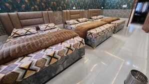 Quarto de hotel com três camas, cada uma com roupa de cama estampada, cabeceira decorativa e piso ladrilhado.