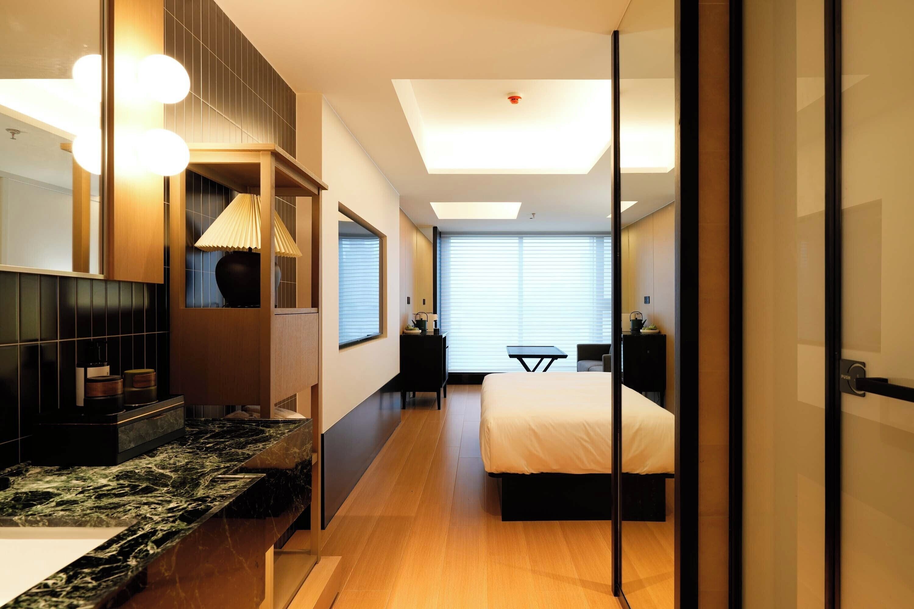Una habitación de hotel moderna con encimera de mármol, cama, escritorio y un amplio ventanal.