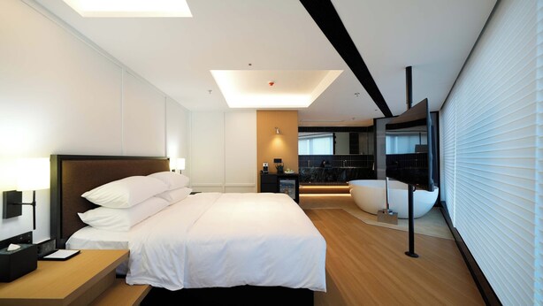 A modern hotel room with a large bed, bedside table, and a view of a cityscape through large windows. - SFEEL Design Hotel Hangzhou Xihu (Hangzhou)