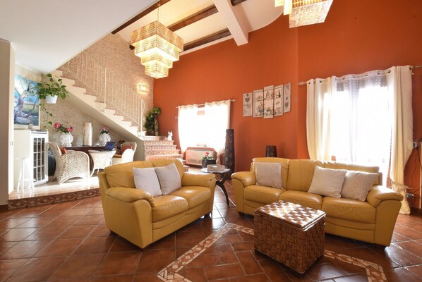 A spacious living area with two yellow sofas, a woven coffee table, a staircase with a view, and a kitchen area. - Vacation Home in Giarratana with 4 bedrooms sleeps 7 (Giarratana)