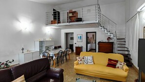 Et flerplans opholdsrum med spiseplads, sofa, trappe og køkken.