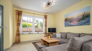 A living room with a sofa, a coffee table, a TV, and a painting on the wall. - Comfortable vacation home Am Deich House 16 with garden and terrace in Zingst - Am (Zingst)
