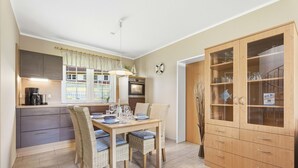 Een compacte keuken met moderne apparatuur, een eethoek met rieten stoelen en een houten kast met glazen deuren.