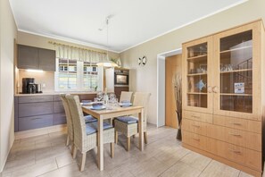 Eine kompakte Küche mit modernen Geräten, ein Essbereich mit Korbstühlen und eine Holzkabine mit Glastüren.