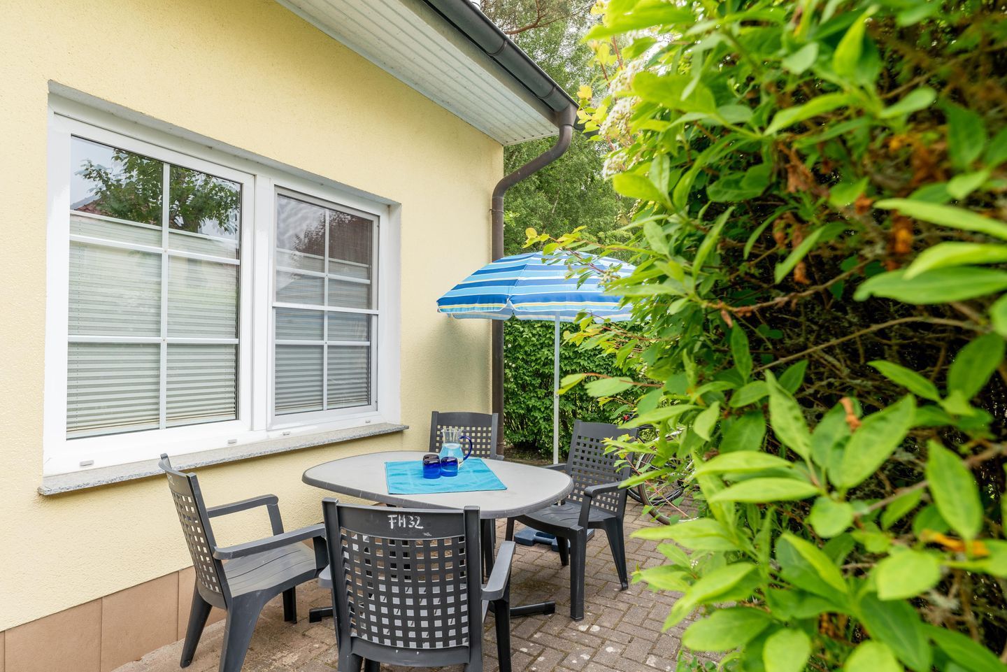 Un patio con una mesa y sillas, una sombrilla azul y una ventana con persianas.