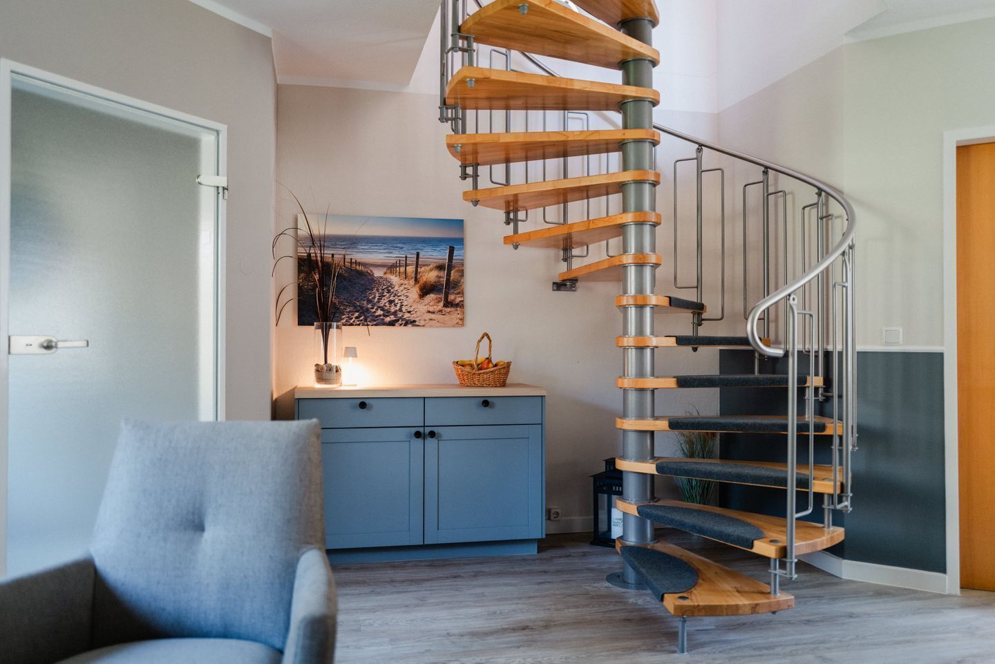 Ein modernes Interieur mit einer Wendeltreppe, einem blauen Schrank und einem Gemälde einer Strandansicht.