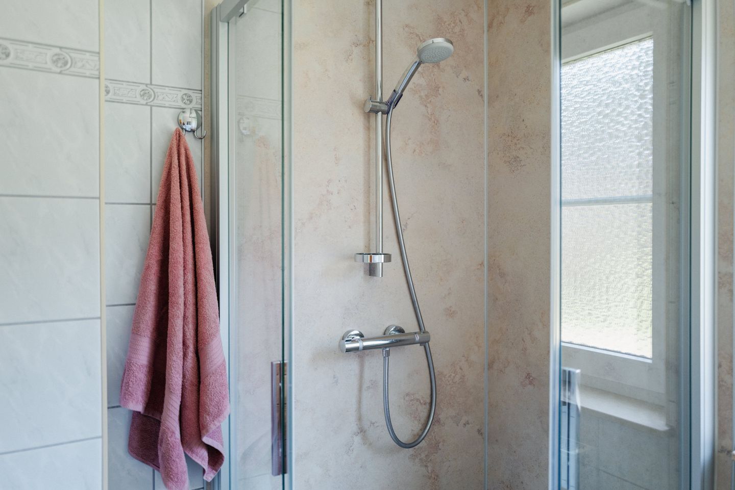 A bathroom with a glass shower enclosure, a visible towel rack, and a window.
