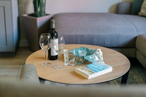 A round wooden table with a bottle of wine, two wine glasses, a book, and a decorative item. - Modern semi-detached house just a few meters from the Baltic Sea beach - Am Deich (Zingst)
