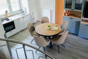 A modern kitchen with white cabinets, a wooden dining table, and a bowl of fruit. - Modern semi-detached house just a few meters from the Baltic Sea beach - Am Deich (Zingst)