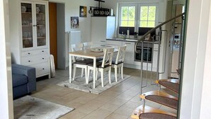 A modern kitchen with a dining area, white cabinetry, and a staircase leading to an upper level. - Family-friendly vacation home near the beach with garden and terrace in Zingst (Zingst)