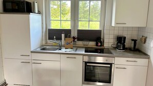 A modern kitchen with white cabinets, a built-in oven, a microwave, a coffee maker, and a window with a view of greenery. - Family-friendly vacation home near the beach with garden and terrace in Zingst (Zingst)