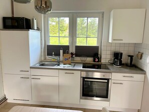 Eine moderne Küche mit weißen Schränken, einem Backofen, einer Mikrowelle, einer Kaffeemaschine und einem Fenster mit Blick auf Grünflächen.