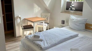 A neatly made bed with white linens and folded towels, a small wooden table with a chair, a bedside lamp, and a window with a sailboat decoration. - Family-friendly vacation home near the beach with garden and terrace in Zingst (Zingst)
