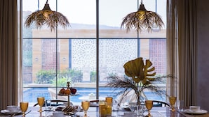 Een eettafel gedekt met gouden glazen, een fruitschaal en uitzicht op een zwembad door grote ramen.