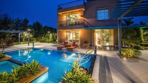 Een modern huis met twee verdiepingen, een zwembad, terrasmeubels buiten en een overdekt terras.