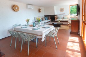 A dining area with a table set for four, surrounded by white chairs. There is a sofa and a fireplace in the background. - Villa Fornaci - Diadema of Venus (Marina di Campo)