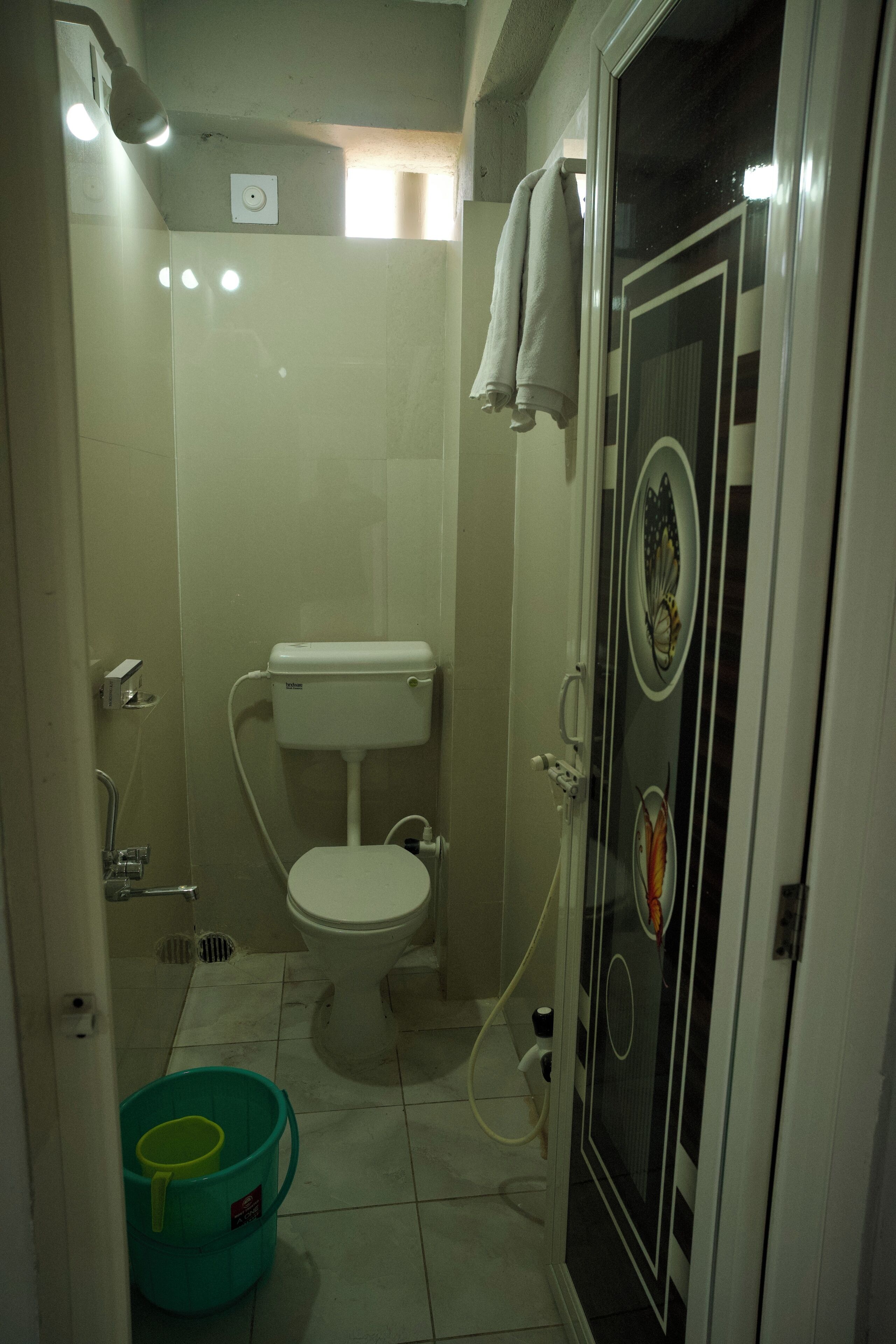 Um banheiro pequeno com vaso sanitário, chuveiro e porta de vidro com adesivo decorativo.