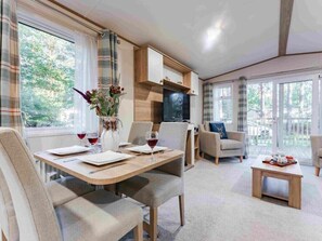 A modern living room with a dining area, large windows, and a fireplace. - Mabel - Kelling Heath Holiday Park - 20957 (Holt)