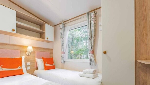 Una habitació d'hotel amb dos llits, una finestra amb cortines, una làmpada i una estanteta sobre els llits.
