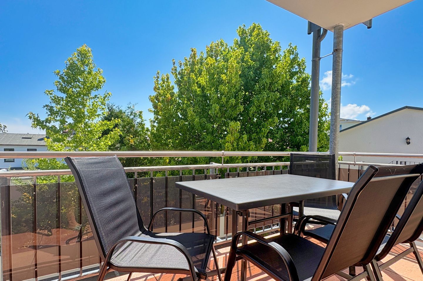 Un balcon avec une table et des chaises, une balustrade et une vue sur les arbres et les bâtiments.