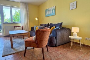 A living room with a sofa, armchair, table, and lamp. - Central but quiet, balcony, free swimming pool and sauna - Villa Elisenhof Elli 5 (Göhren)